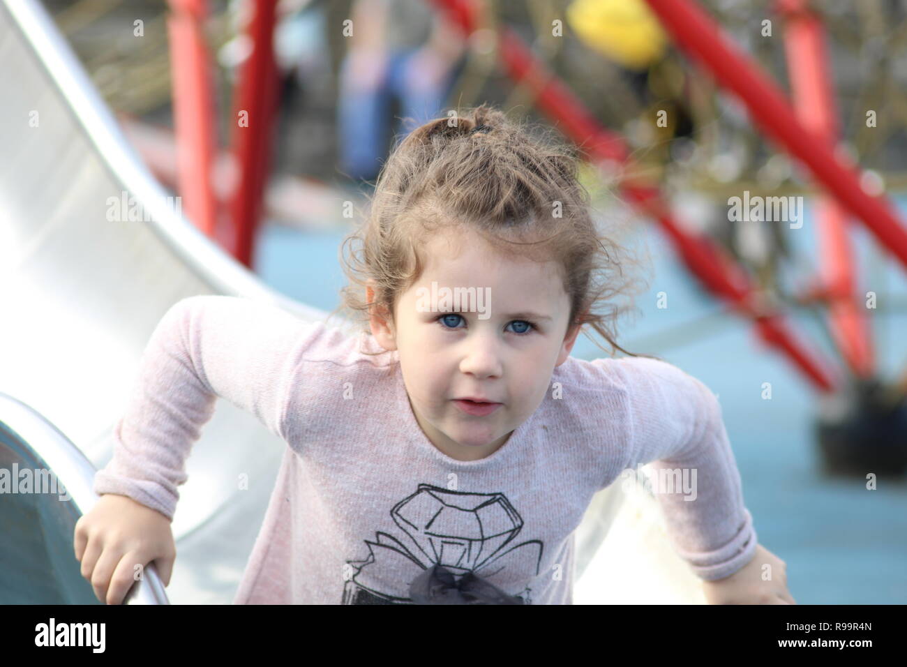 Young girl with brown hair and blue eyes getting up of a slide in a park in skegness Stock Photo