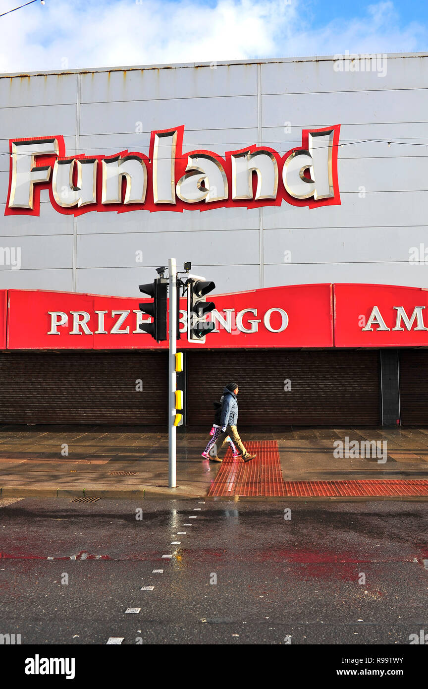 Two people walking along the Promenade in front of a closed Funland amusement arcade on a wet day in winter in Blackpool Stock Photo