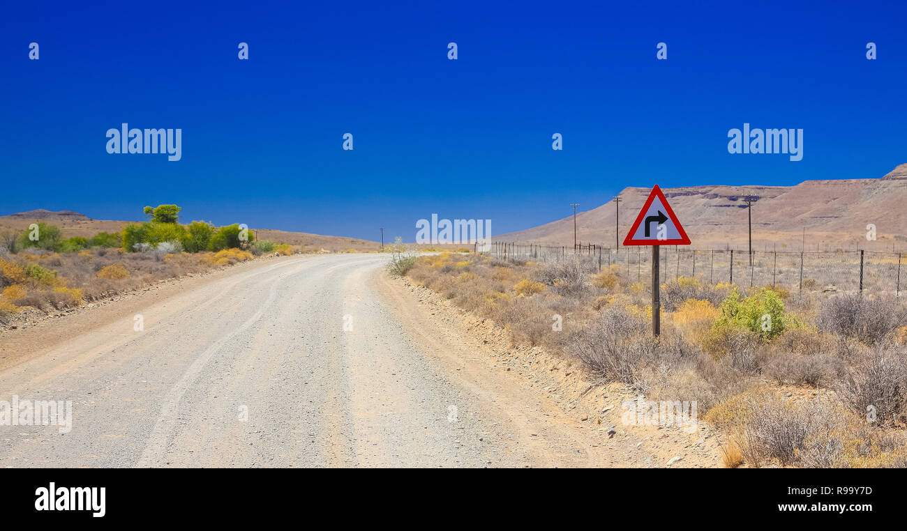 Desert landscape view of a sharp left turn sign on a dirt road in the Karoo of South Africa Stock Photo