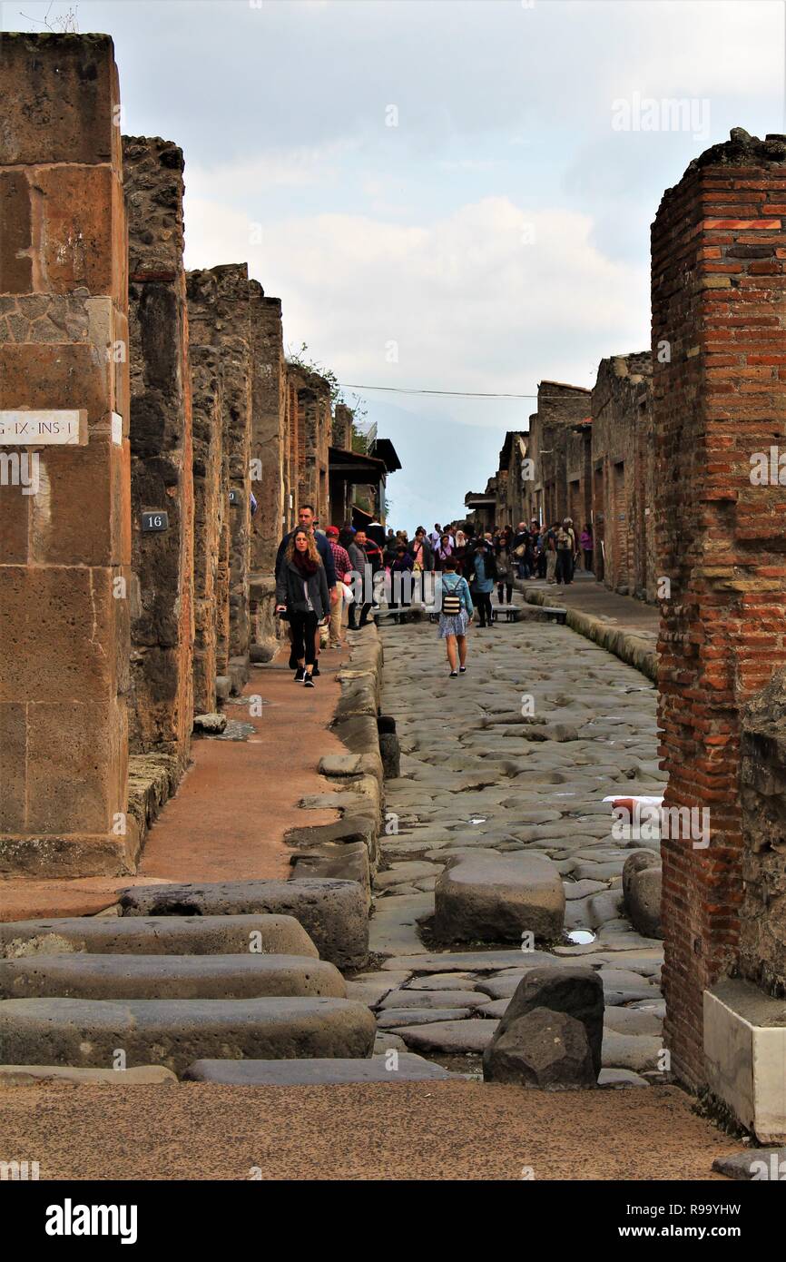 Pompeii, Italy - October 23rd 2018: Tourists survey and explore one of the many streets within the ruins of the ancient city of Pompeii. Stock Photo