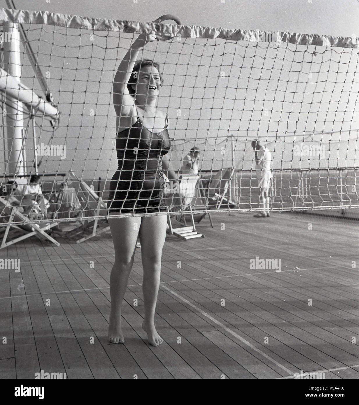 1950s, historical, on board the union-castle steamship 'Kenya', a lady passenger in her swimsuit outside on the ship's wooden deck playing a throwing game over a net. Stock Photo