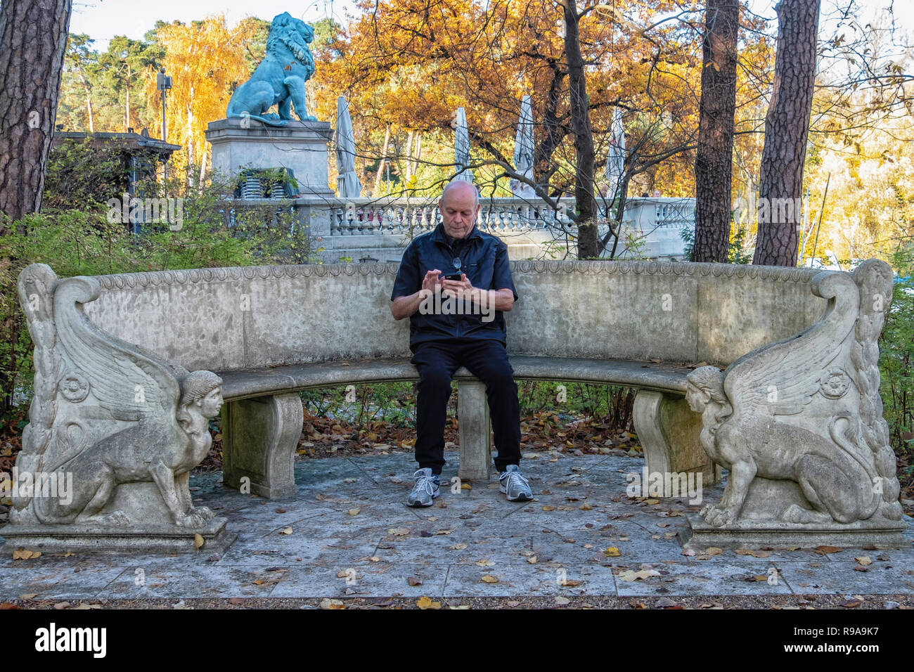 Berlin. Old man sits on decorartive bench in garden of House of the Wannsee Conference Memorial Site with Flensburg Lion in background.. Stock Photo