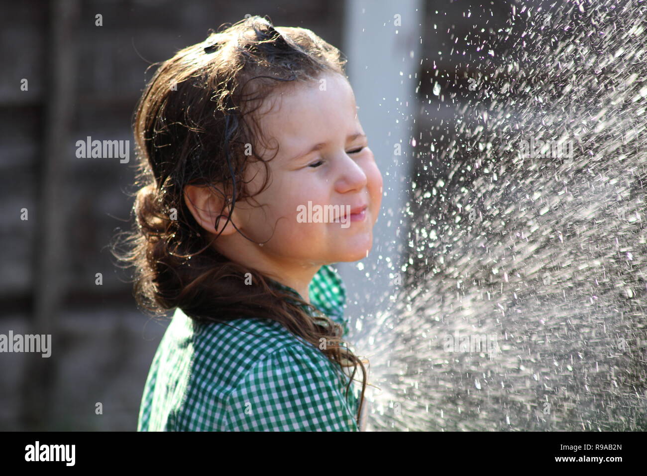 young child girl playing with a hose pipe and spraying water in her face Stock Photo