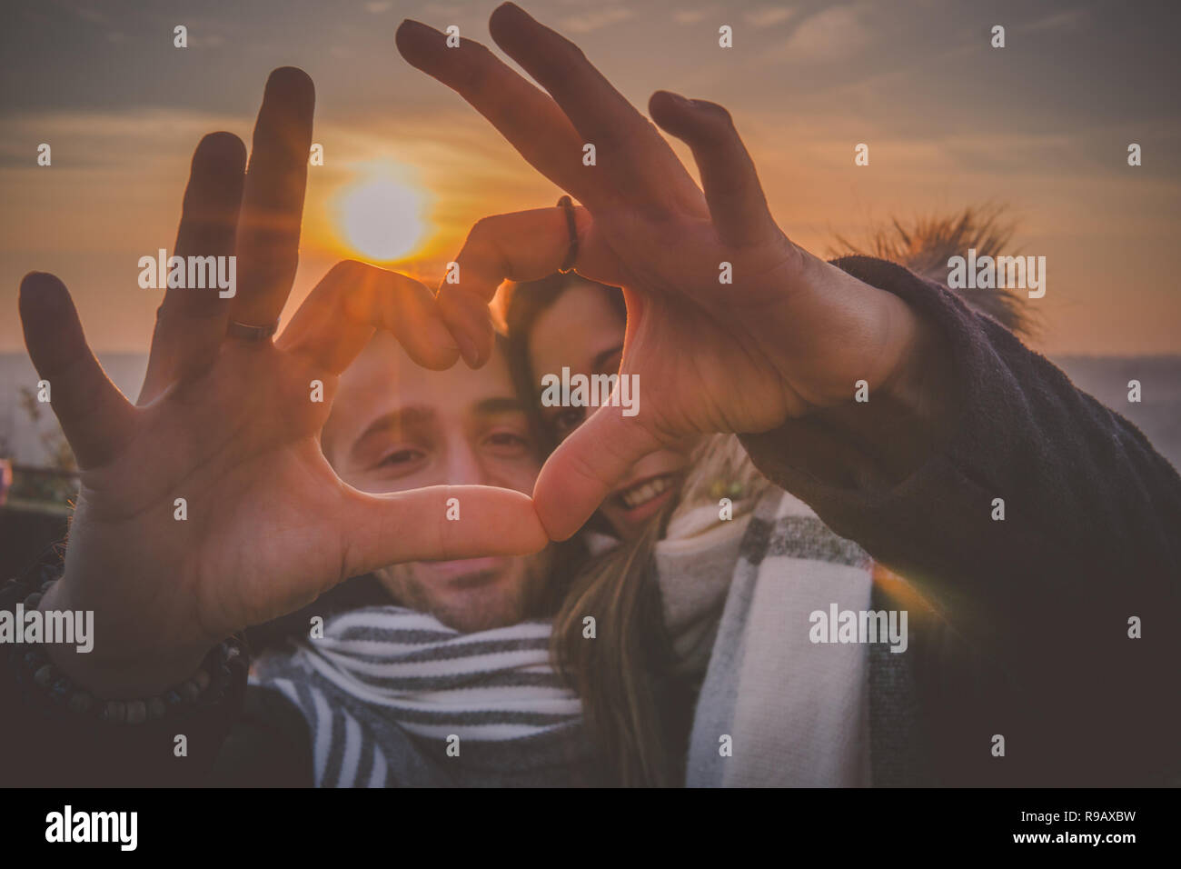 Young couple in love making heart shape with hands in the sunset moment Stock Photo