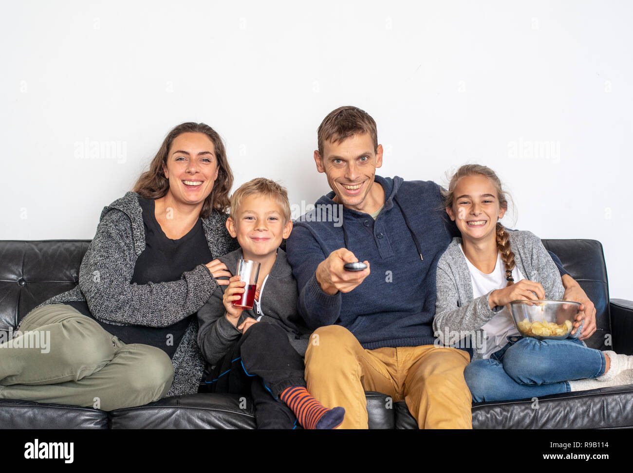 young family watching TV indoors. Front view people sitting on sofa looking at television. Stock Photo