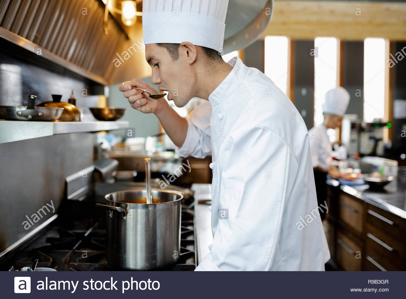 Chef tasting sauce at stove in restaurant kitchen Stock Photo Alamy