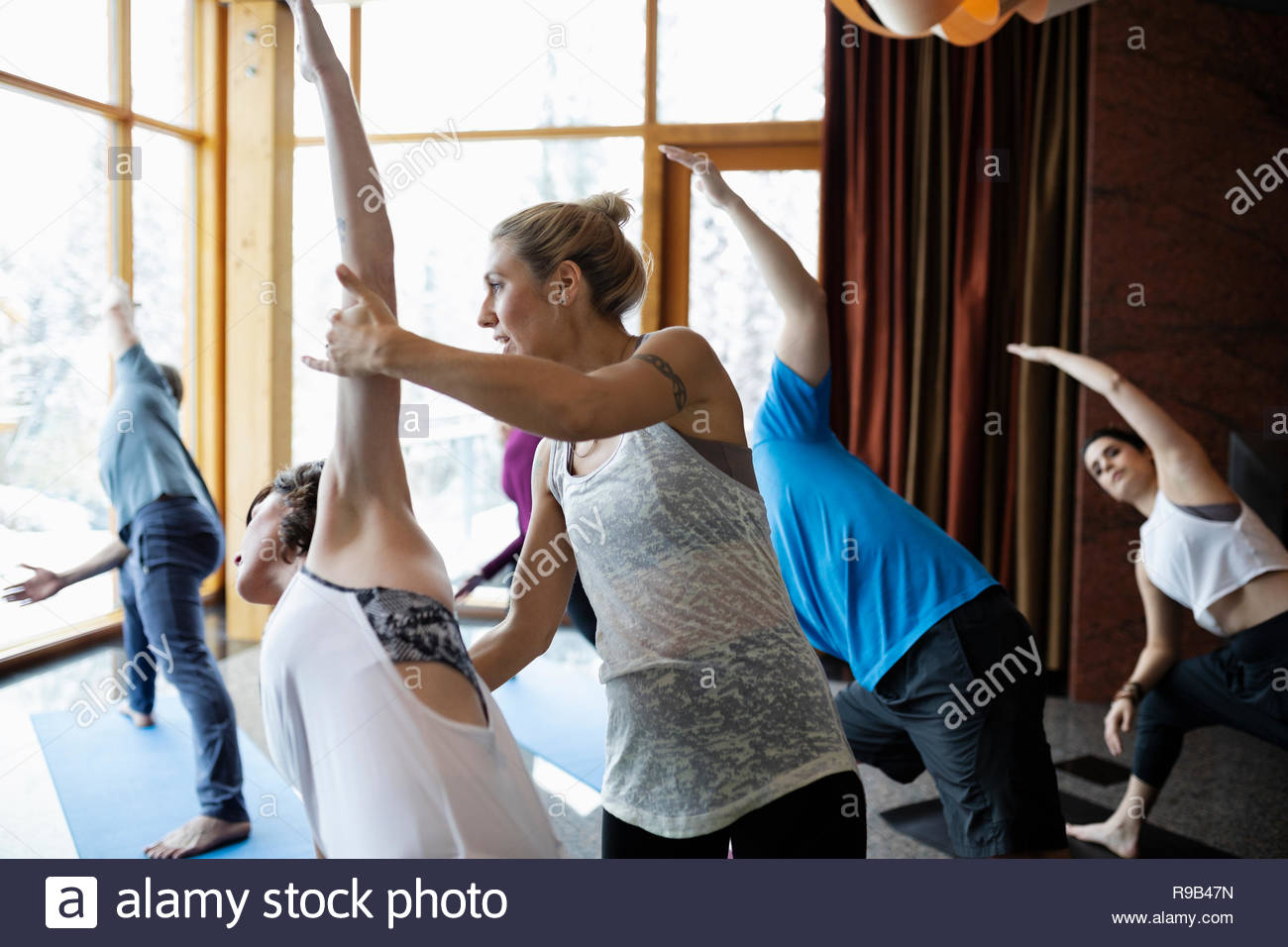 Instructor supporting woman practicing side angle pose in yoga class studio Stock Photo