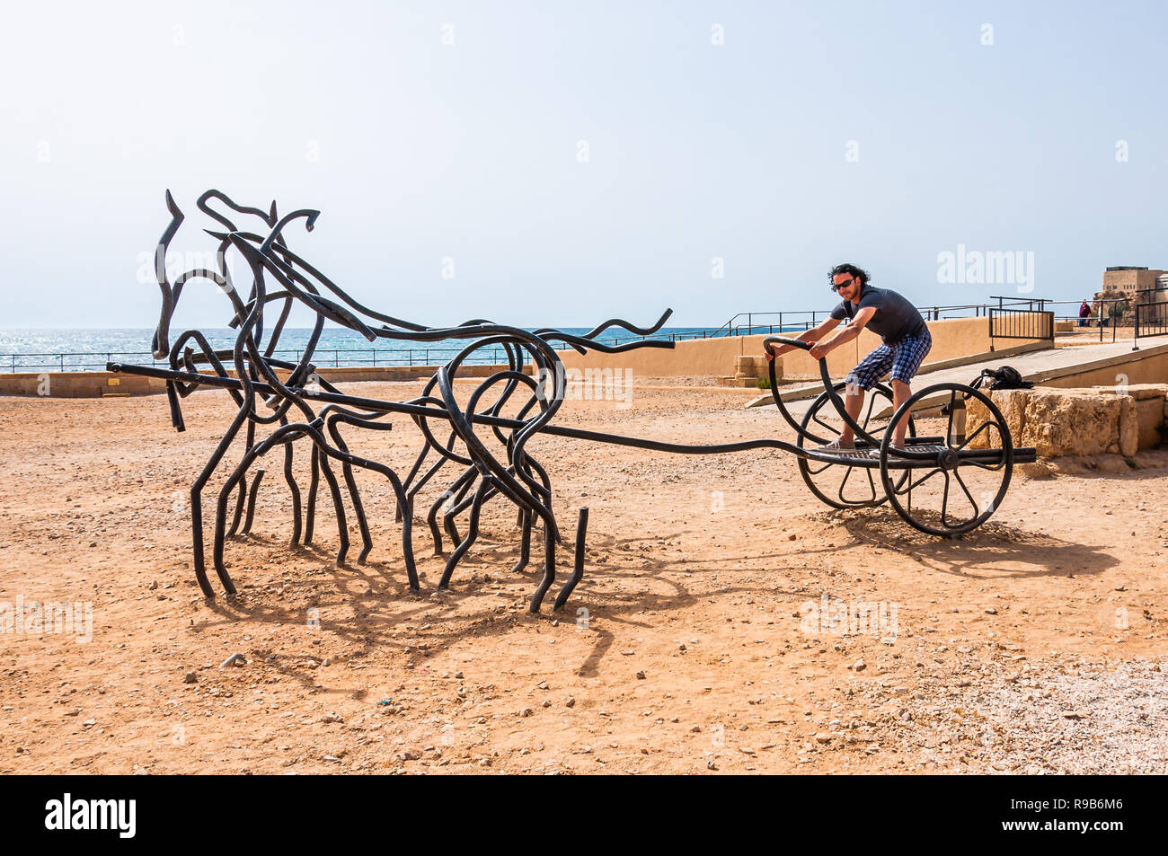 Caesarea, Israel - May 22, 2012: Tourist man standing on modern sculpture of Roman Horse Chariot made of black bent forged metal stand on ancient Caes Stock Photo