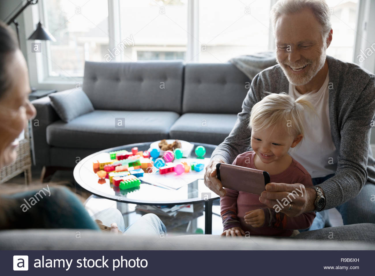 Grandfather and granddaughter using smart phone in living room Stock Photo