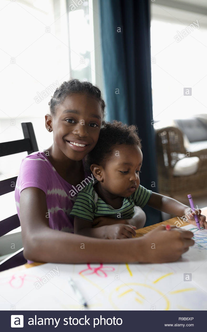 Portrait smiling girl holding brother in lap and coloring at table Stock Photo