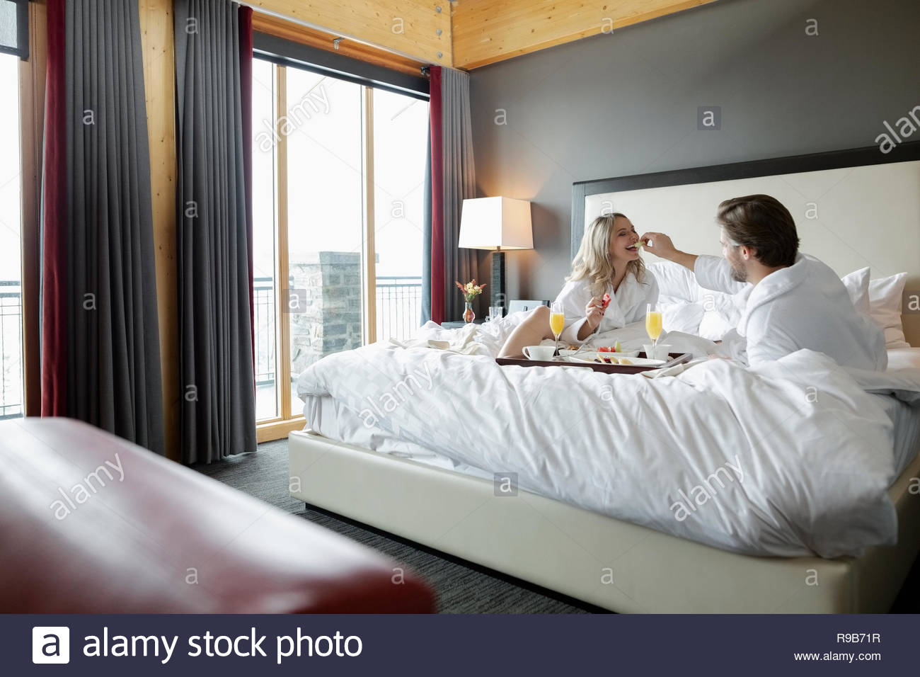 Couple In Bathrobes Enjoying Breakfast In Bed In Luxury
