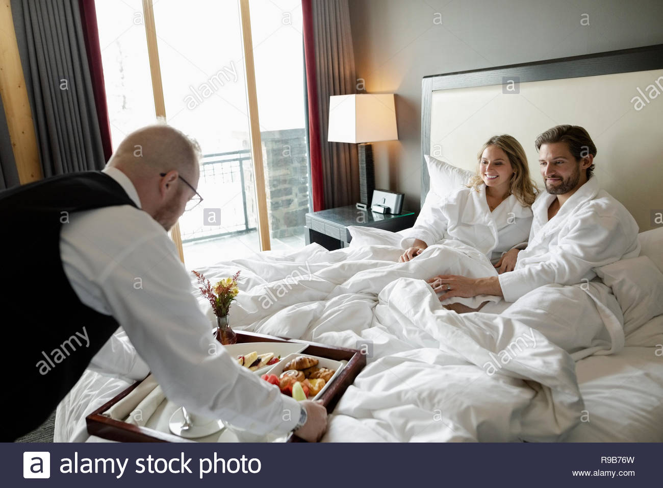 Room service hotel staff waiter serving breakfast to couple in