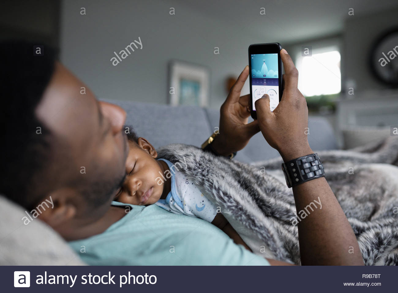 Father using smart phone with baby son sleeping on chest Stock Photo