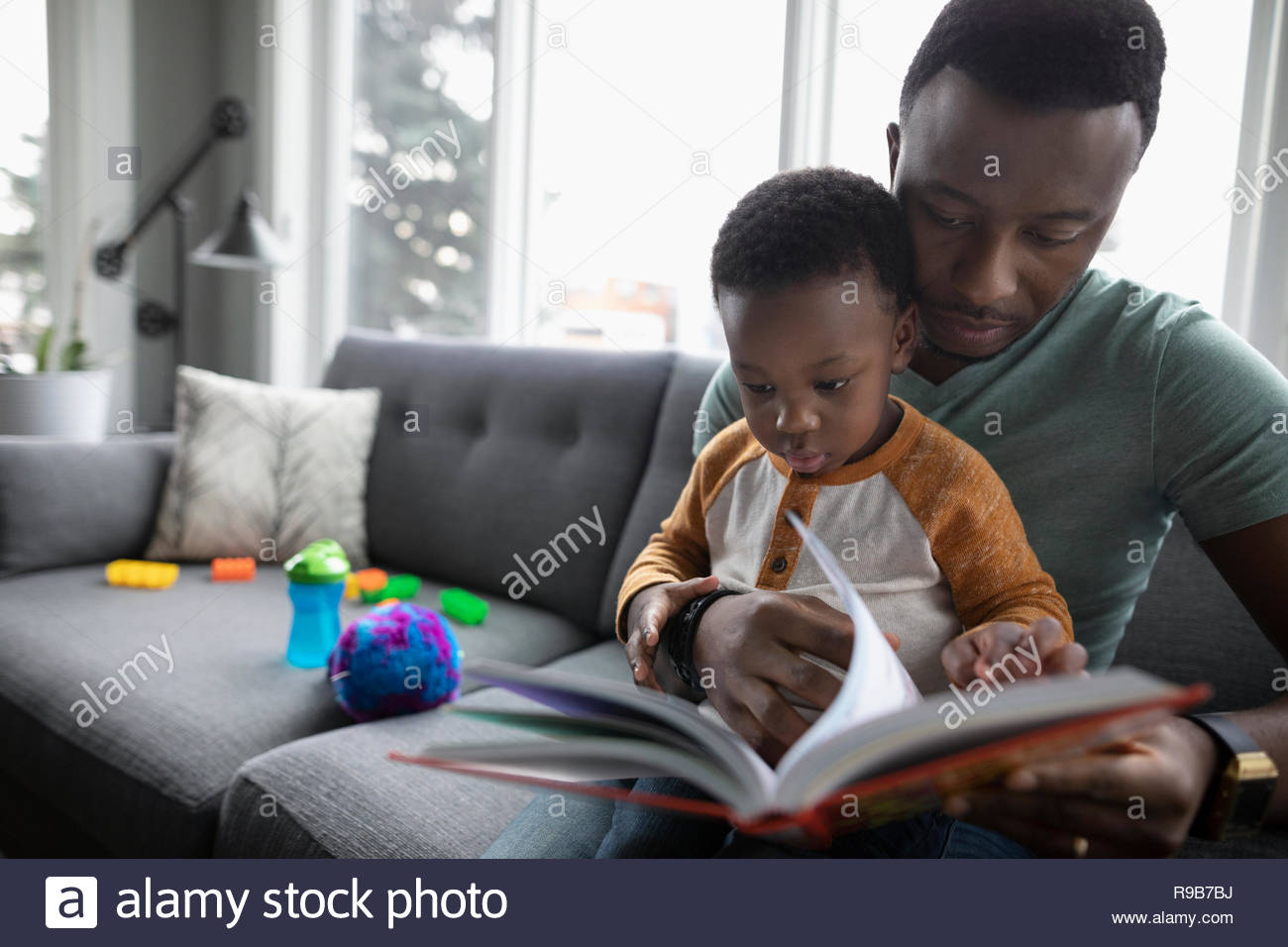 Father and toddler son reading book on living room sofa Stock Photo