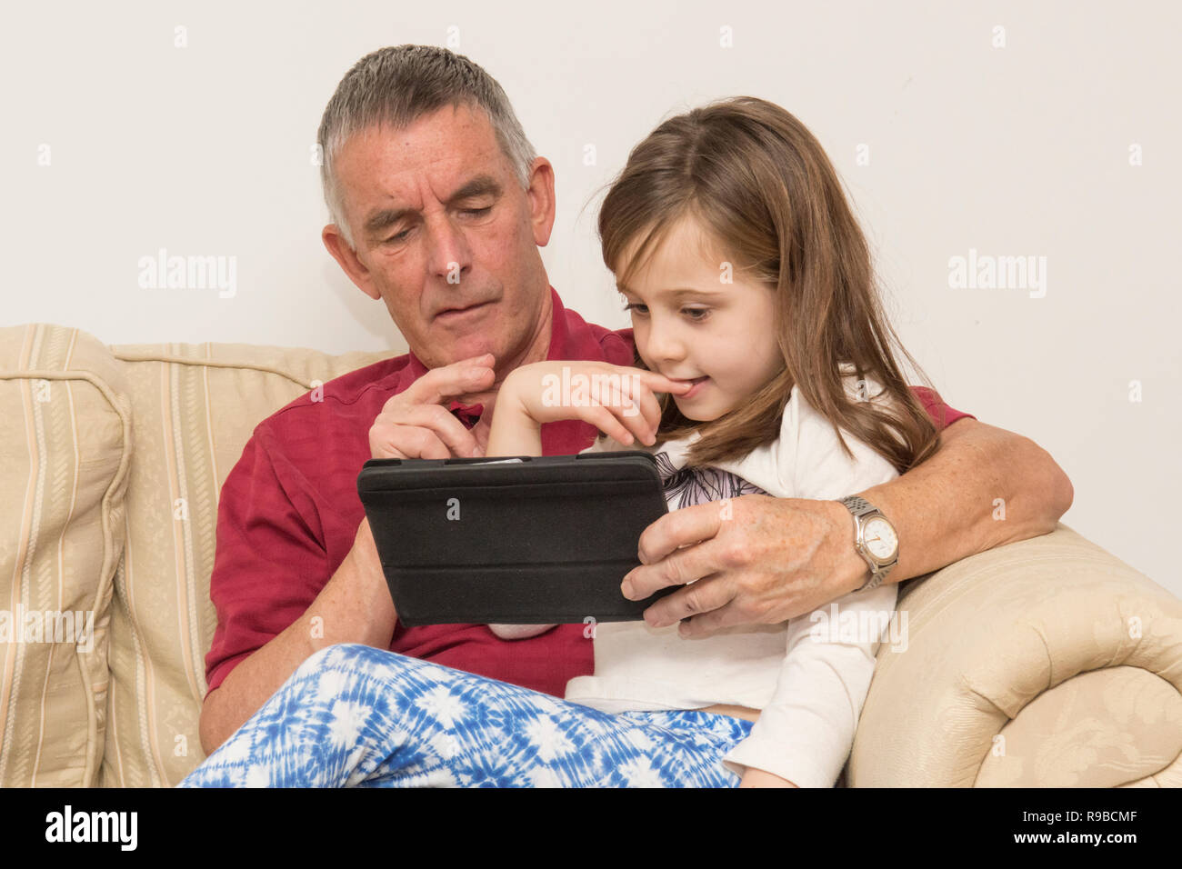 granddaughter  helping grandfather with tablet, electronic device, social media, modern technology. girl helping ageing father with iPad, tablet. Stock Photo