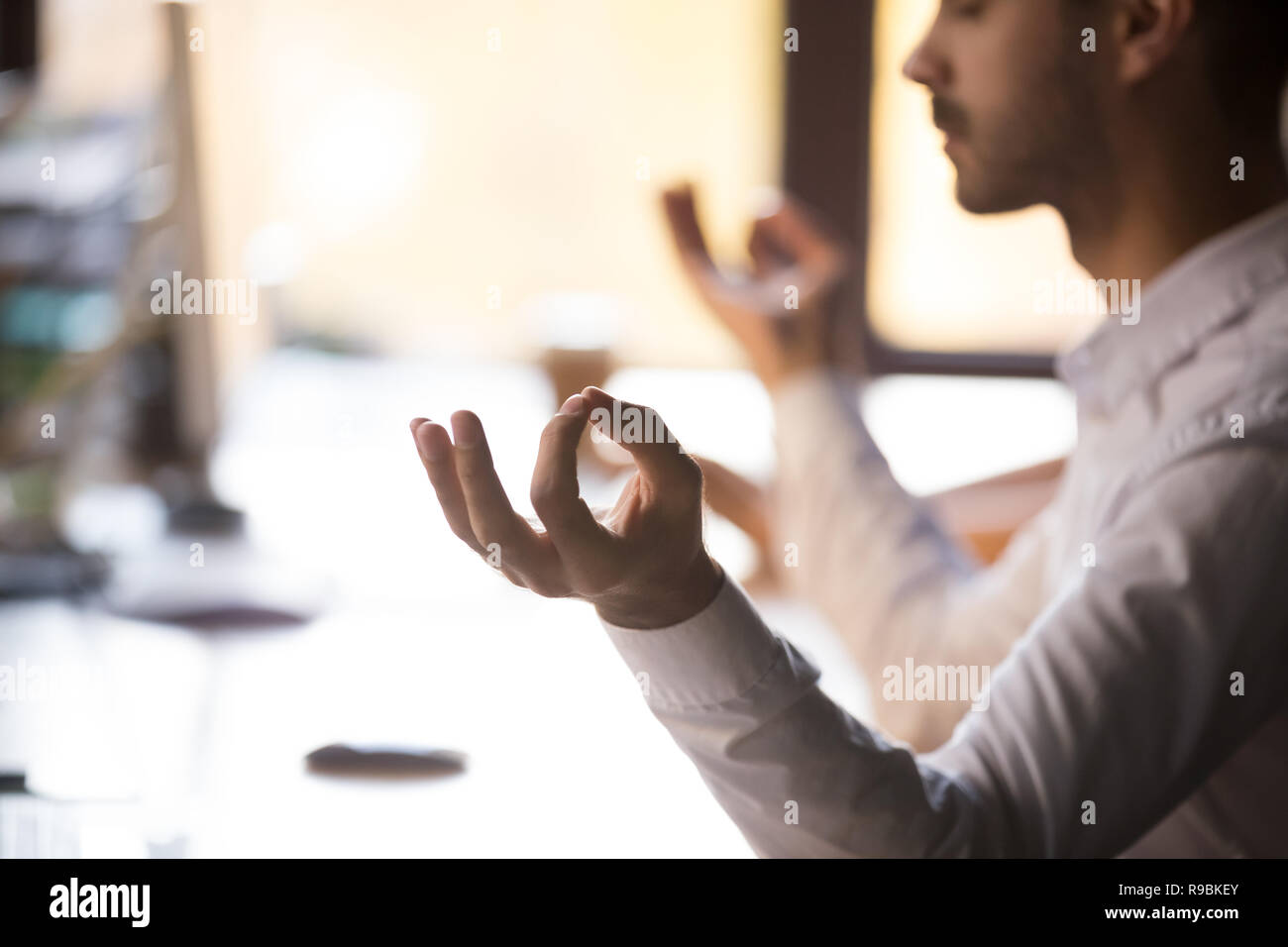 Man sitting at desk holding hands in mudra meditating, closeup Stock Photo