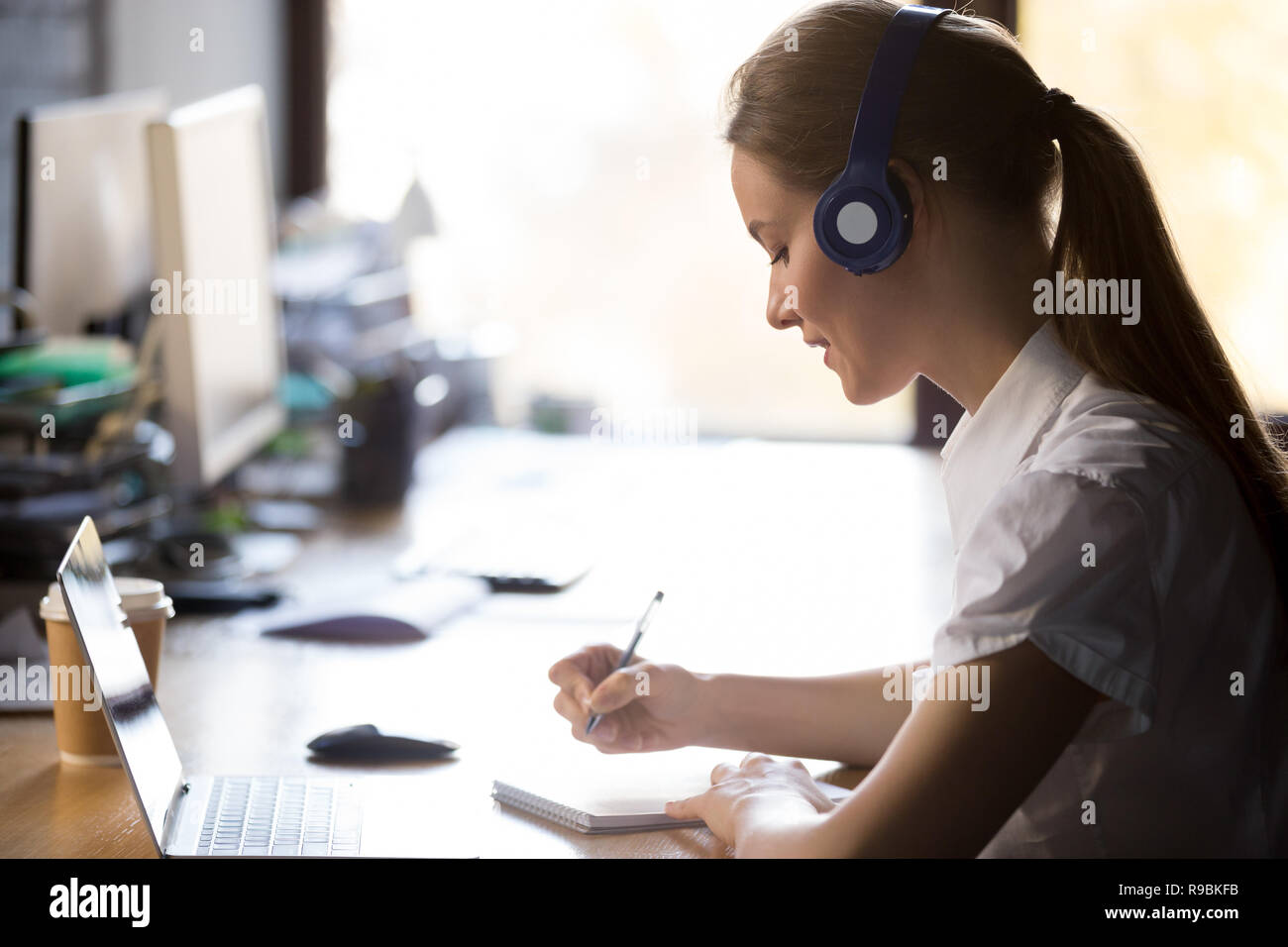 Focused woman wearing headphones write notes study online with t Stock Photo