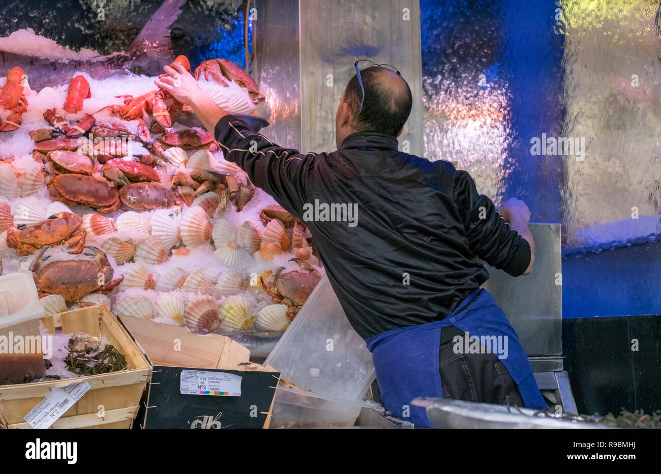 A fish monger arranges a display of fresh shellfish, including lobsters, crabs and scallops, on a bed of ice for sale in a nearby restaurant. Stock Photo