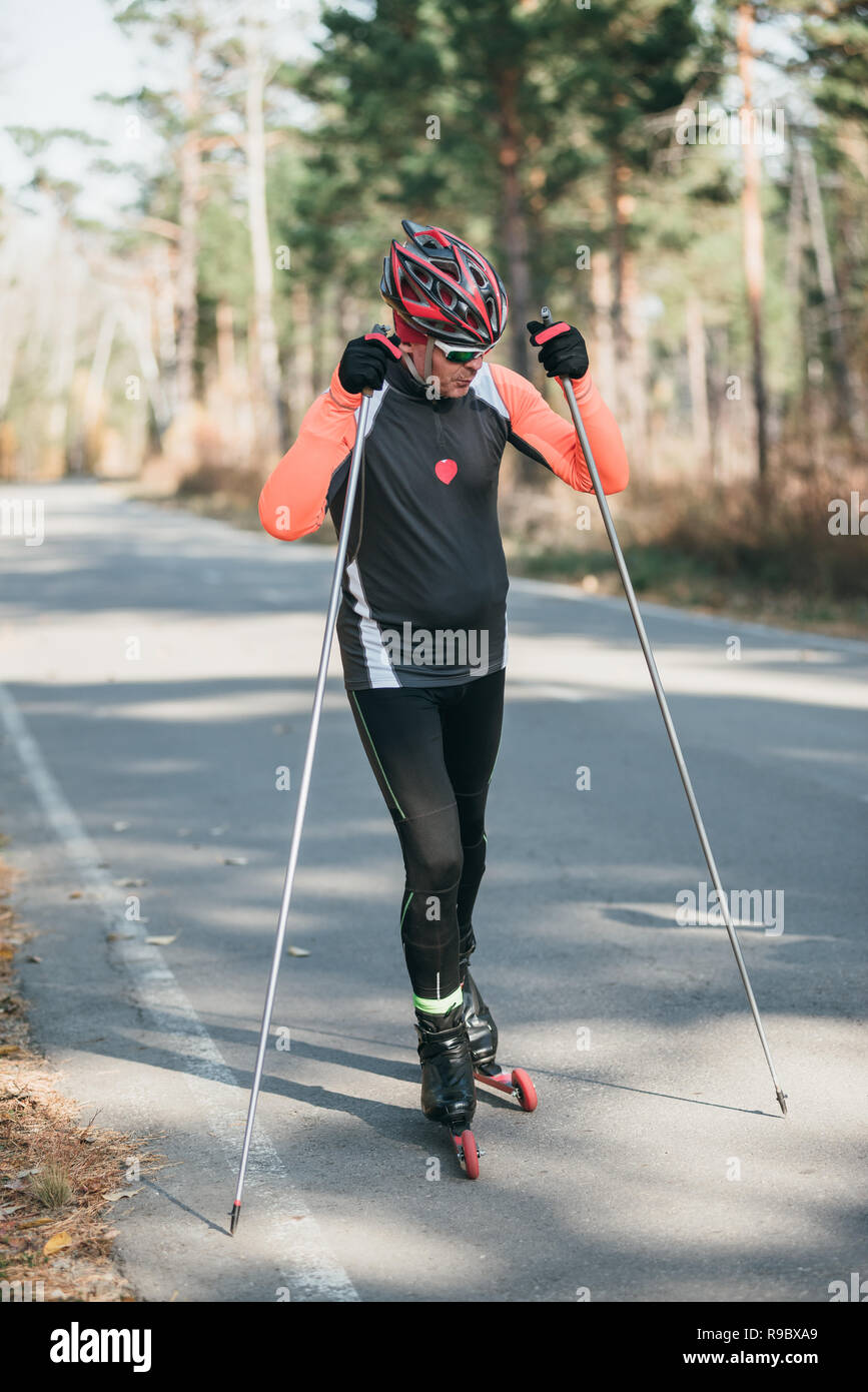 Training an athlete on the roller skaters. Biathlon ride on the roller skis  with ski poles, in the helmet. Athlete is getting ready to start. Autumn  workout. Roller sport Stock Photo -