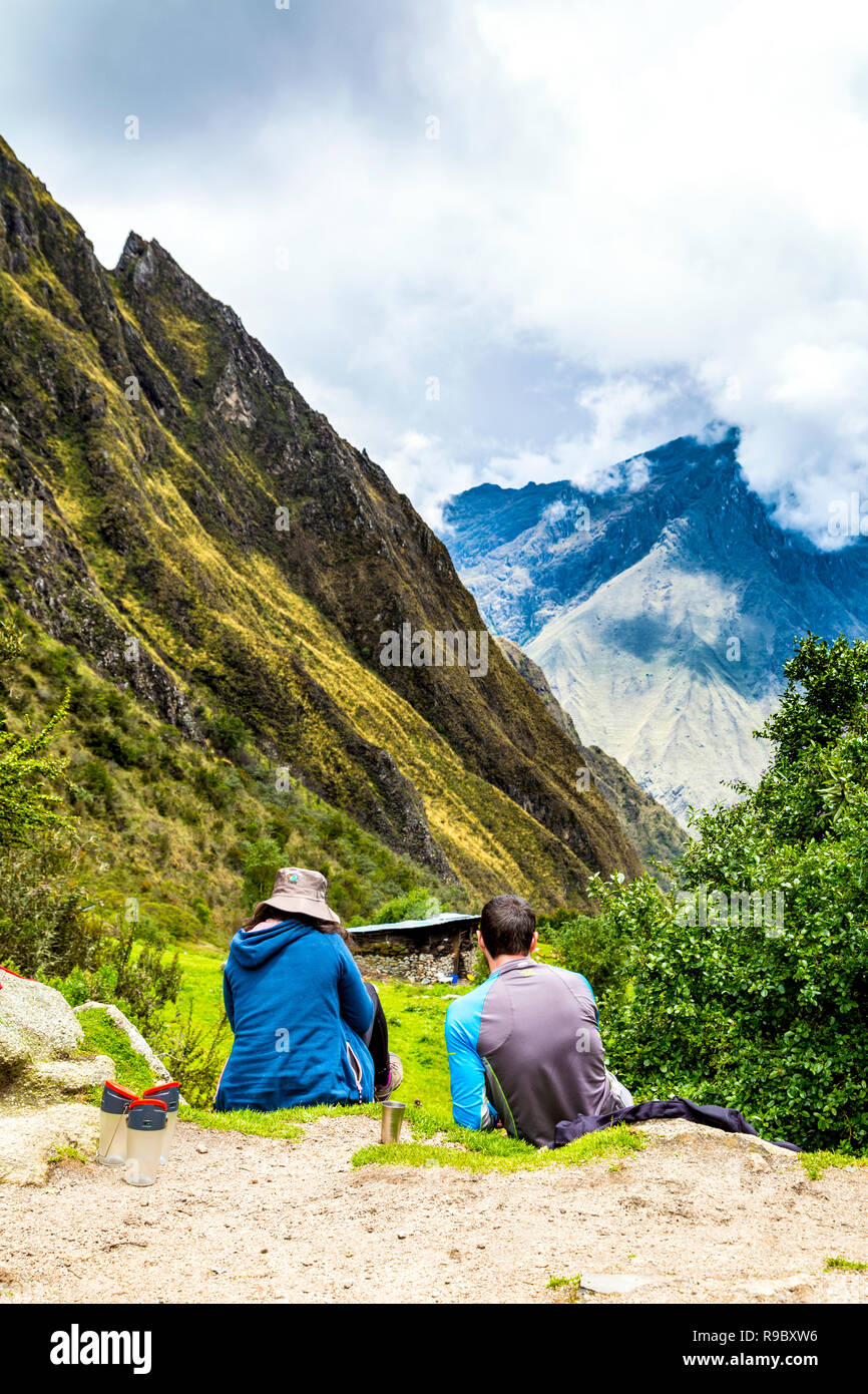 Couple of hikers sitting, resting at lunchbreak, looking at scenic mountain landscape during the Inca Trail to Machu Picchu, Sacred Valley, Peru Stock Photo