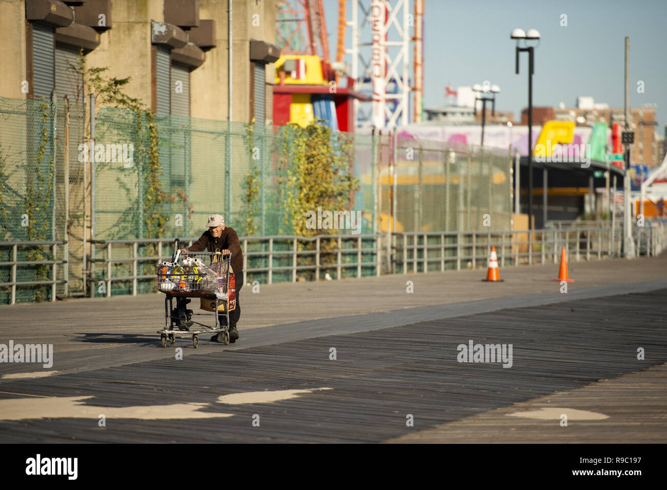 A homeless man is pushing a shopping cart full of stuff collected on Coney Island beach. Stock Photo