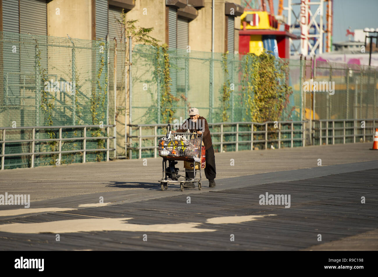 A homeless man is pushing a shopping cart full of stuff collected on Coney Island beach. Stock Photo