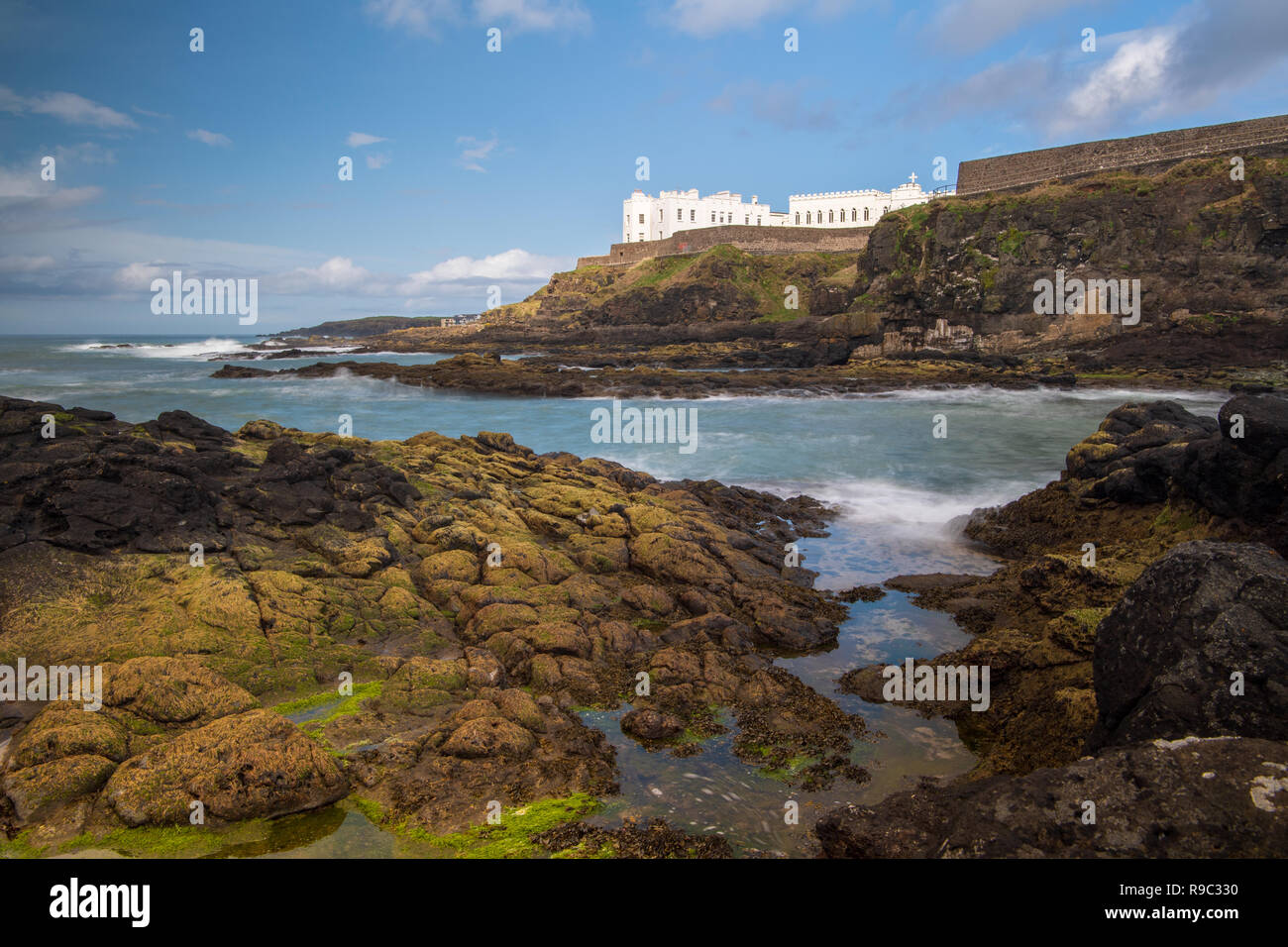 Cliff walk at Port Stewart, Northern Ireland with the Dominican College visible on the clifftop and lichen and seagrass covered rocks in the foreground. Stock Photo