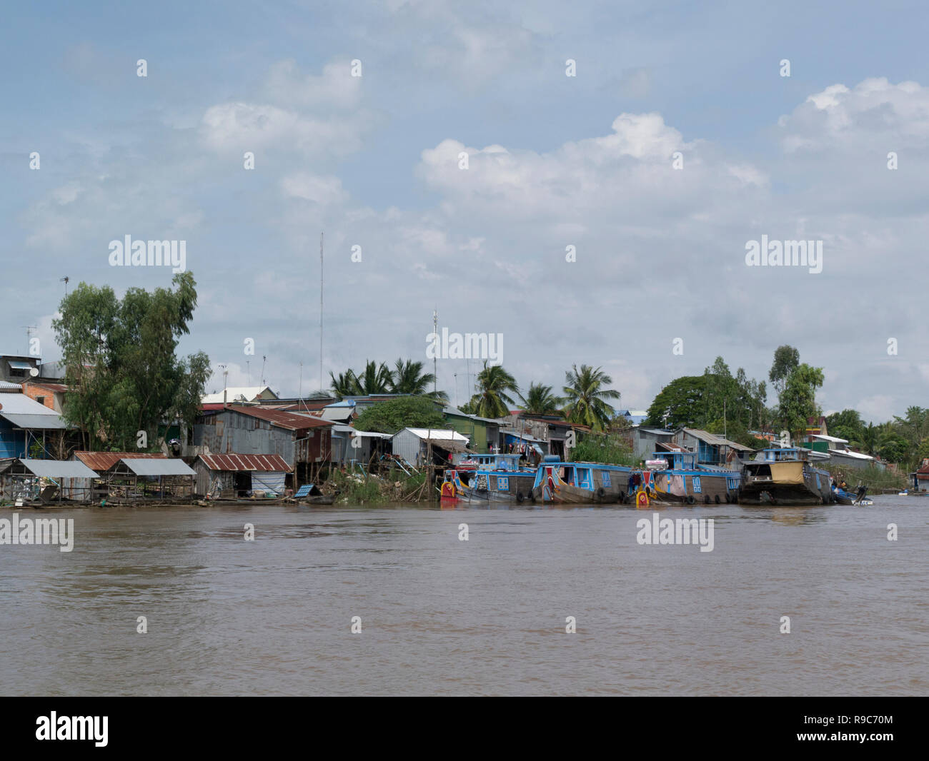 Cambodian village at side of Mekong River viewed from ferry  boat on journey from Chau Doc Vietnam to Phnom Penh Cambodia Asia sampans and wooden rive Stock Photo