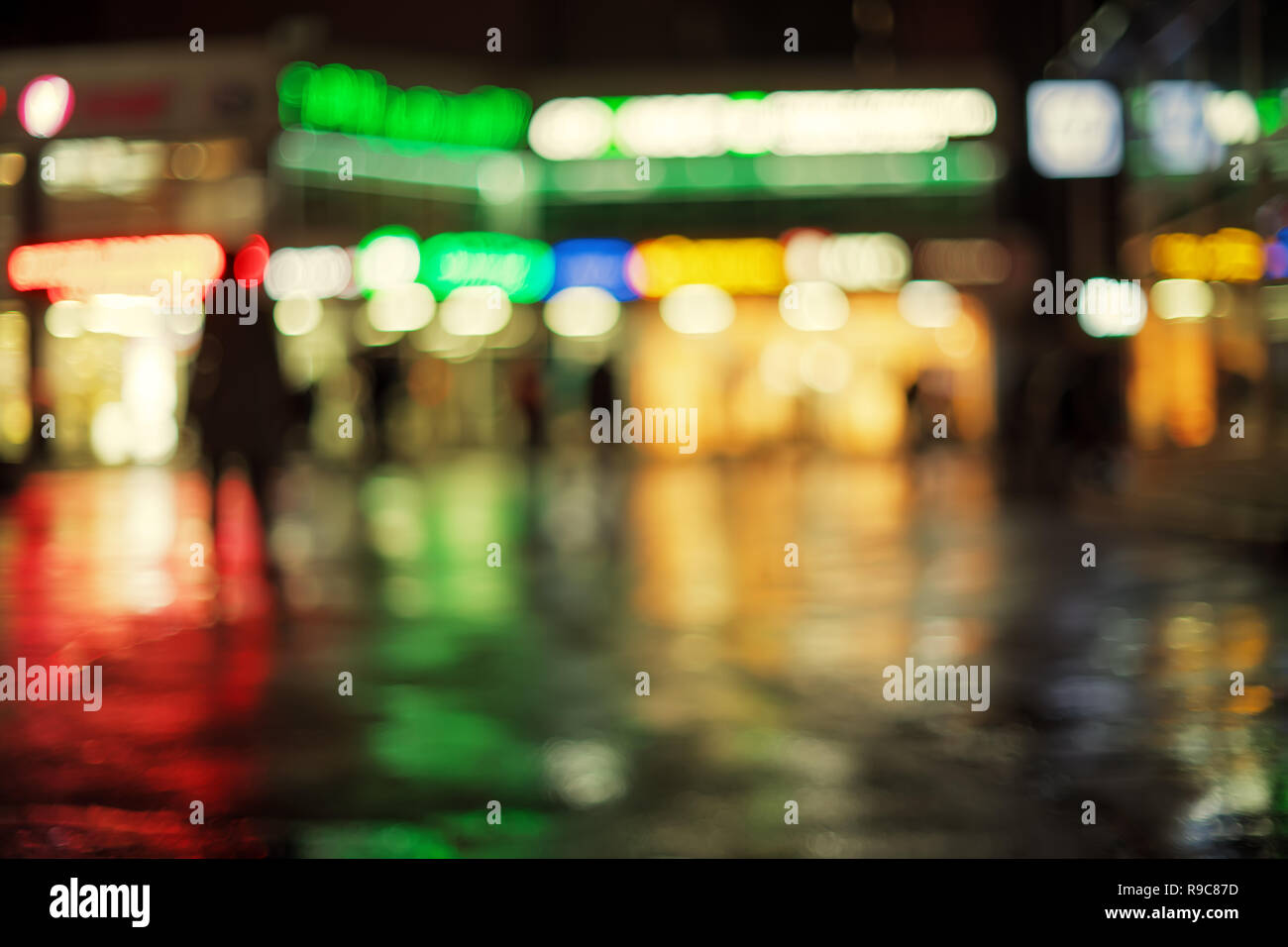 Distant defocused shops windows and their reflections into wet pavement. Abstract blurred background Stock Photo