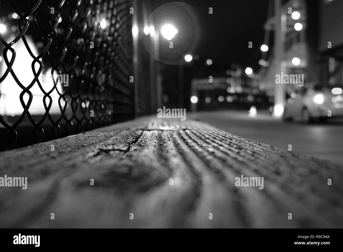 Image of a wooden plank at night with a street light glow, chain link  fence, and car in the distance; low perspective and vanishing focal point  Stock Photo - Alamy