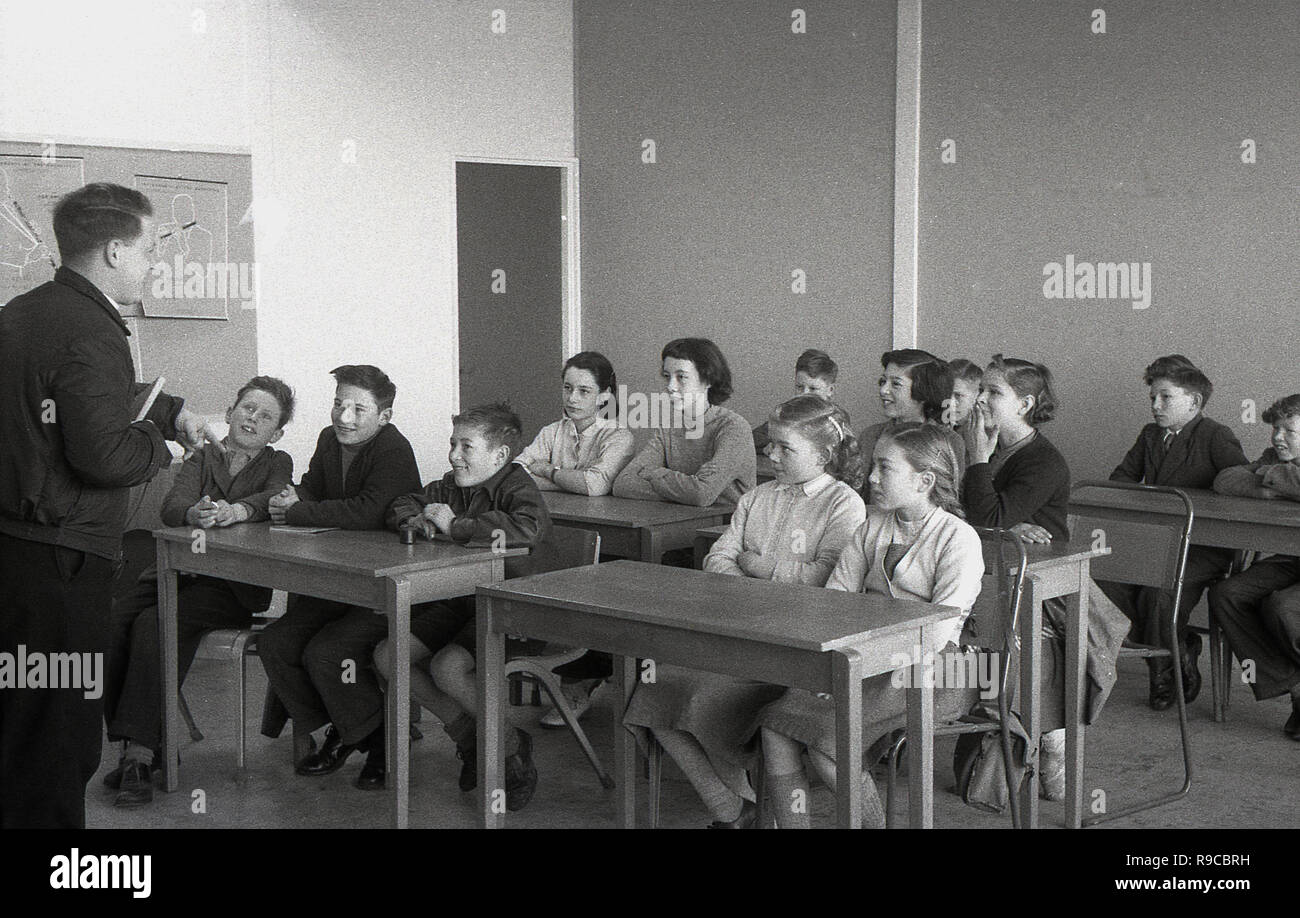 1955, historical, group of primary school children in a classroom, sitting at desks, being taught by a young adult male teacher, who is talking directly with the children,  infront of them and not at a blackboard, England, UK Stock Photo