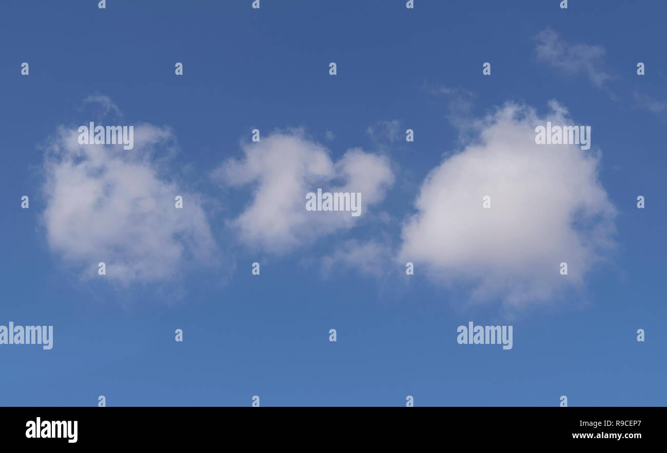 three fluffy white cotton ball clouds in a clear blue sky Stock Photo