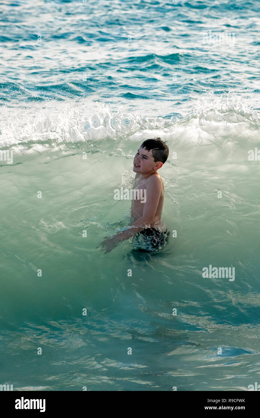 Boys play in ocean on vacation in Caribbean sea - boy in waves in Aruba aquamarine and blue ocean water Stock Photo