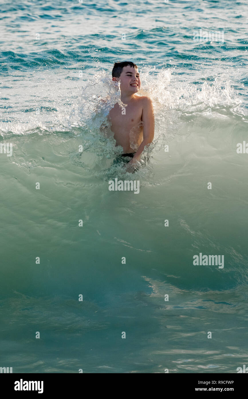 Boys play in ocean on vacation in Caribbean sea - boy in waves in Aruba aquamarine and blue ocean water Stock Photo