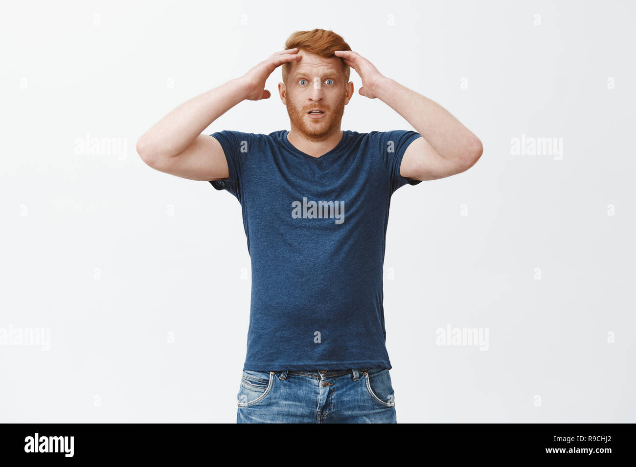 Frustrated gloomy redhead male in blue t-shirt, holding head and staring with disappointment at camera, losing bet, feeling devestation and regret, standing over gray background unhappy Stock Photo