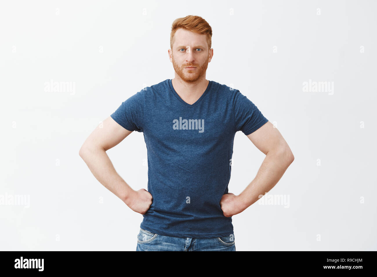 Tell me truth, I am listening. Serious strict and handsome redhead boyfriend in blue t-shirt, holding hands on waist and staring at camera, scolding someone or giving directions, being bossy Stock Photo