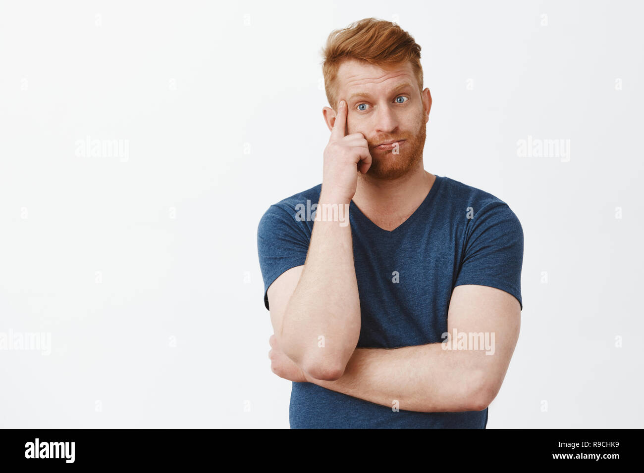 Man losing mind hearing arguments. Distressed tired and fed up handsome redhead mature male with bristle, breathing out, holding finger on temple and looking down with annoyed and troubled expression Stock Photo