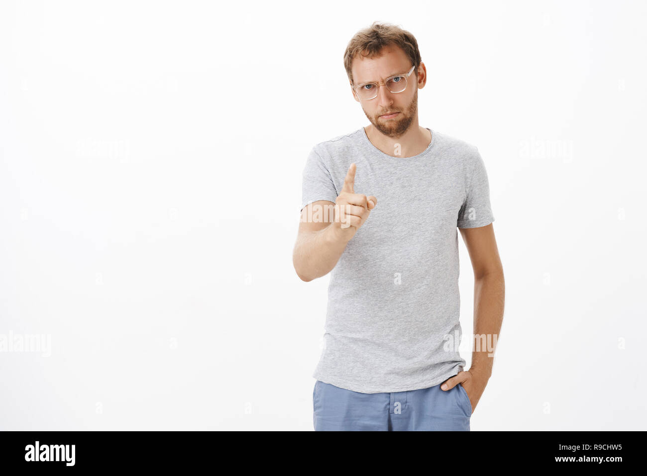 Focused male entrepreneur giving directions on duty being strict and serious with employees shaking index finger, pointing at camera, dissatisfied or disappointed with bad work over white wall Stock Photo