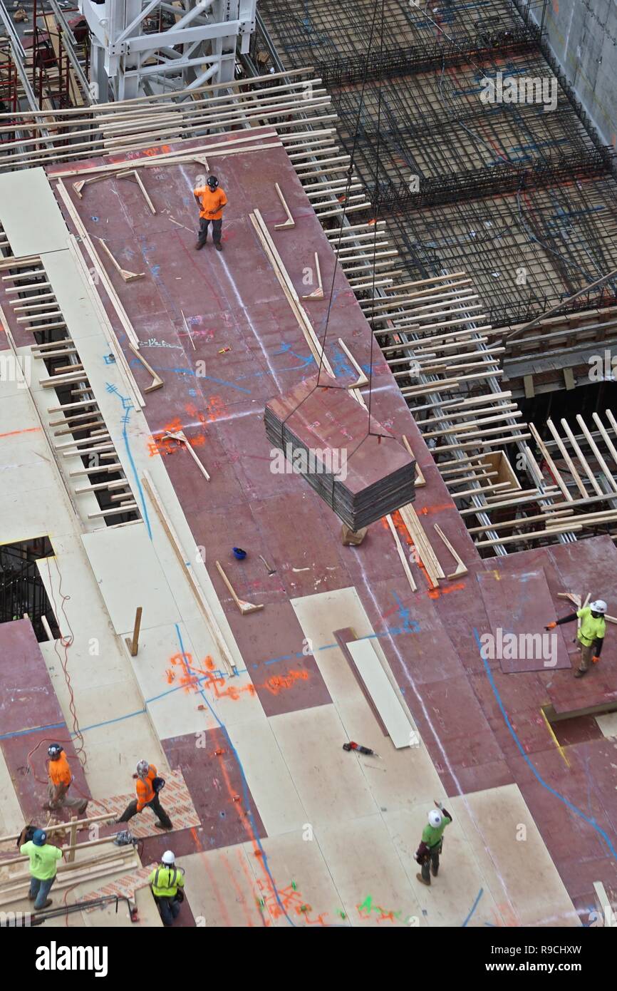 Workmen guiding the delivery of plywood sheets for the construction of