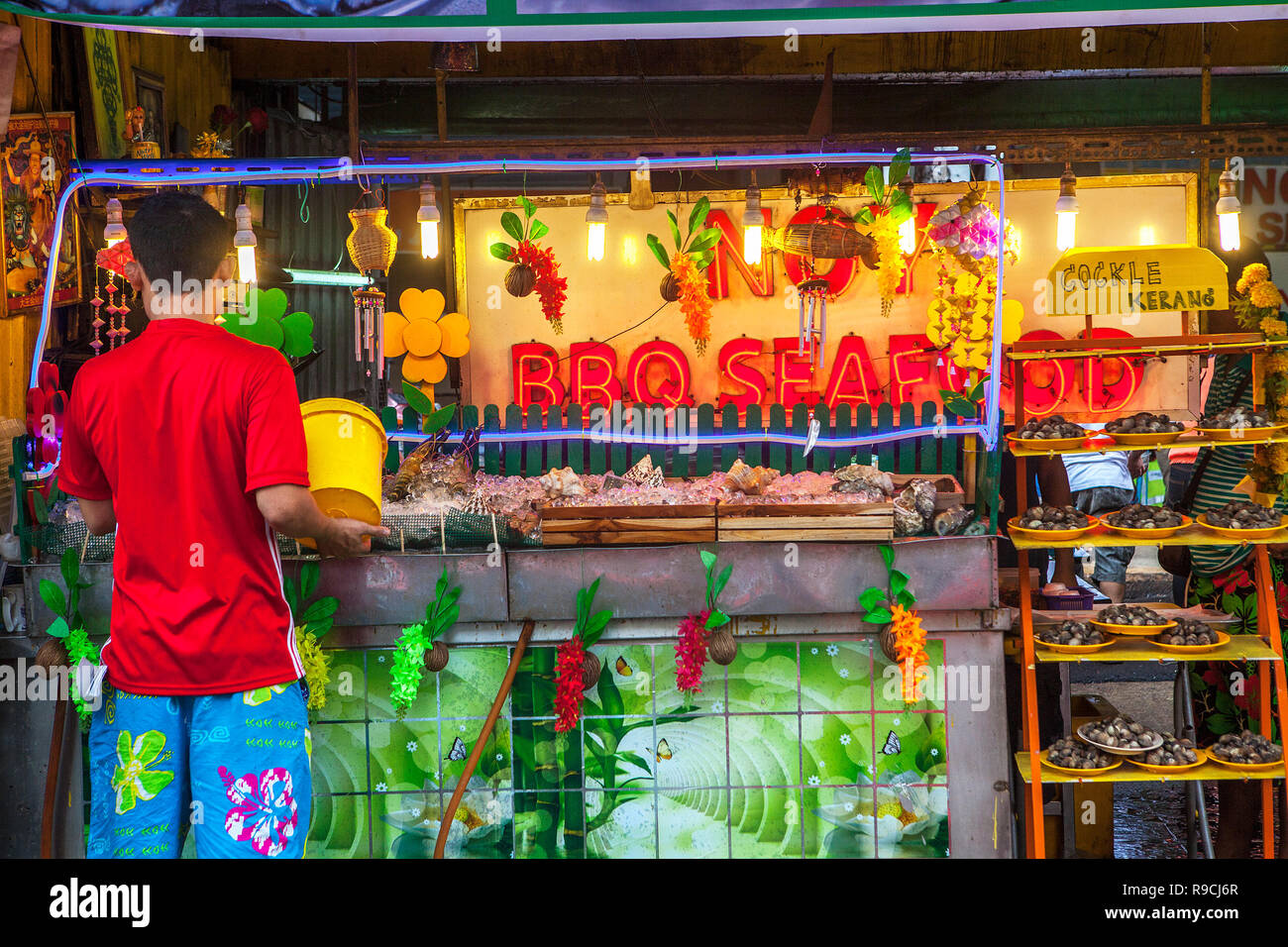 Man selling seafood at his sidewalk food stall advertising with neon lights and signs at Bukit Bintang, Kuala Lumpur, Malaysia. Stock Photo