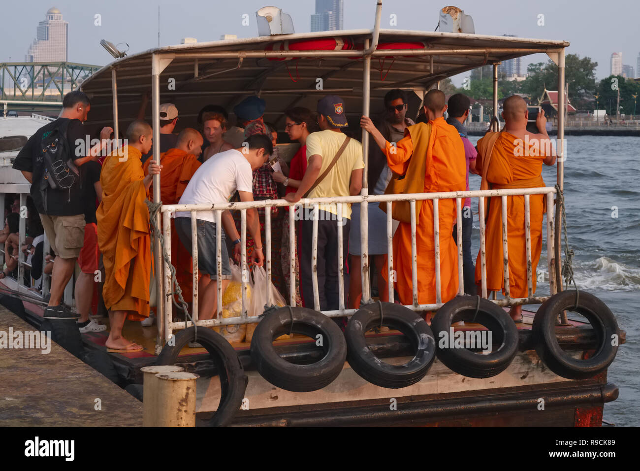 Buddhist monks, other local passengers and tourists on an express boat on the Chao Phraya River, Bangkok, Thailand Stock Photo