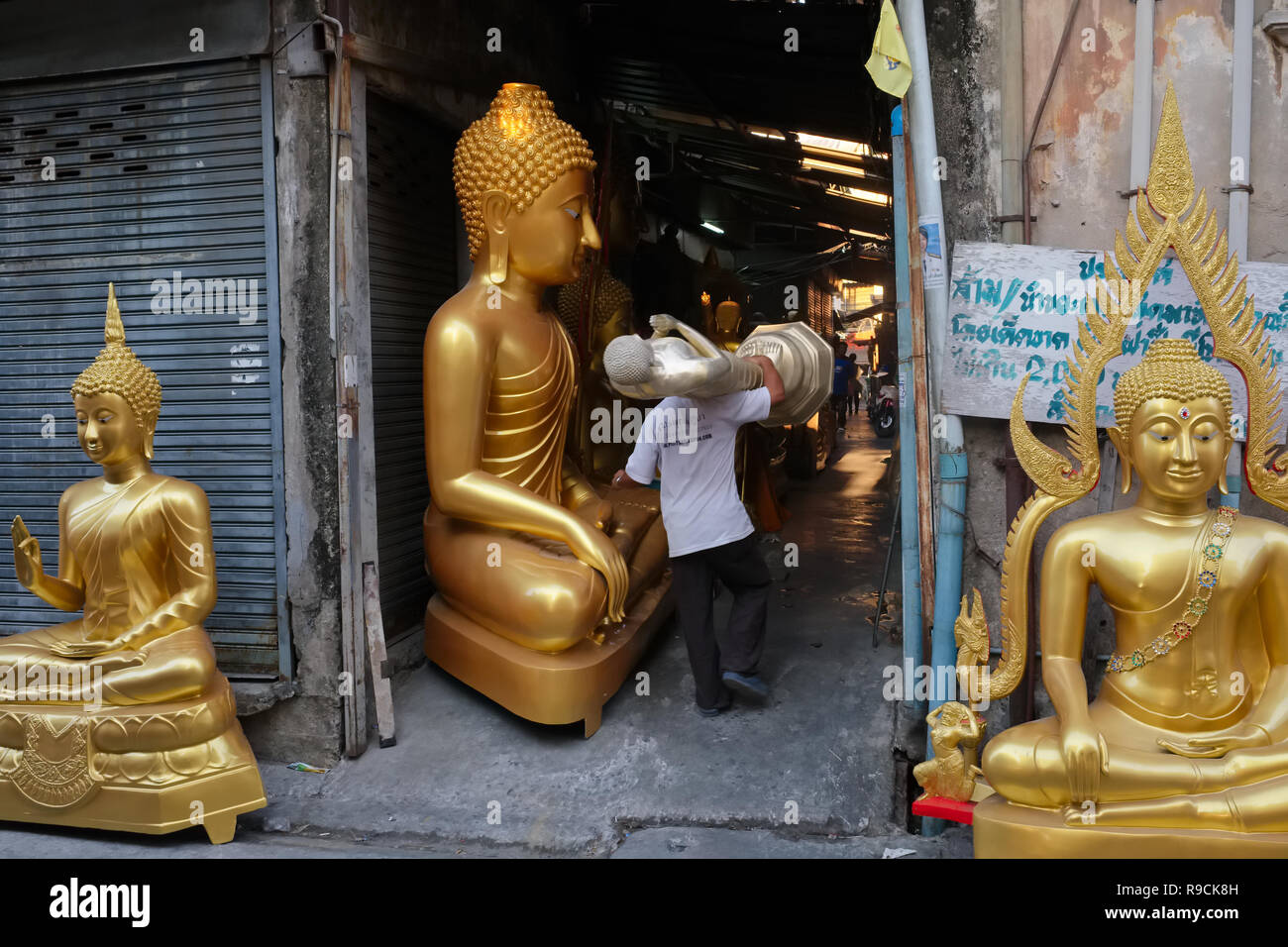 In a factory for Buddha statues in Bamrung Muang Road, Bangkok, Thailand, an employee carries a half-finished statue, passing other Buddha statues Stock Photo