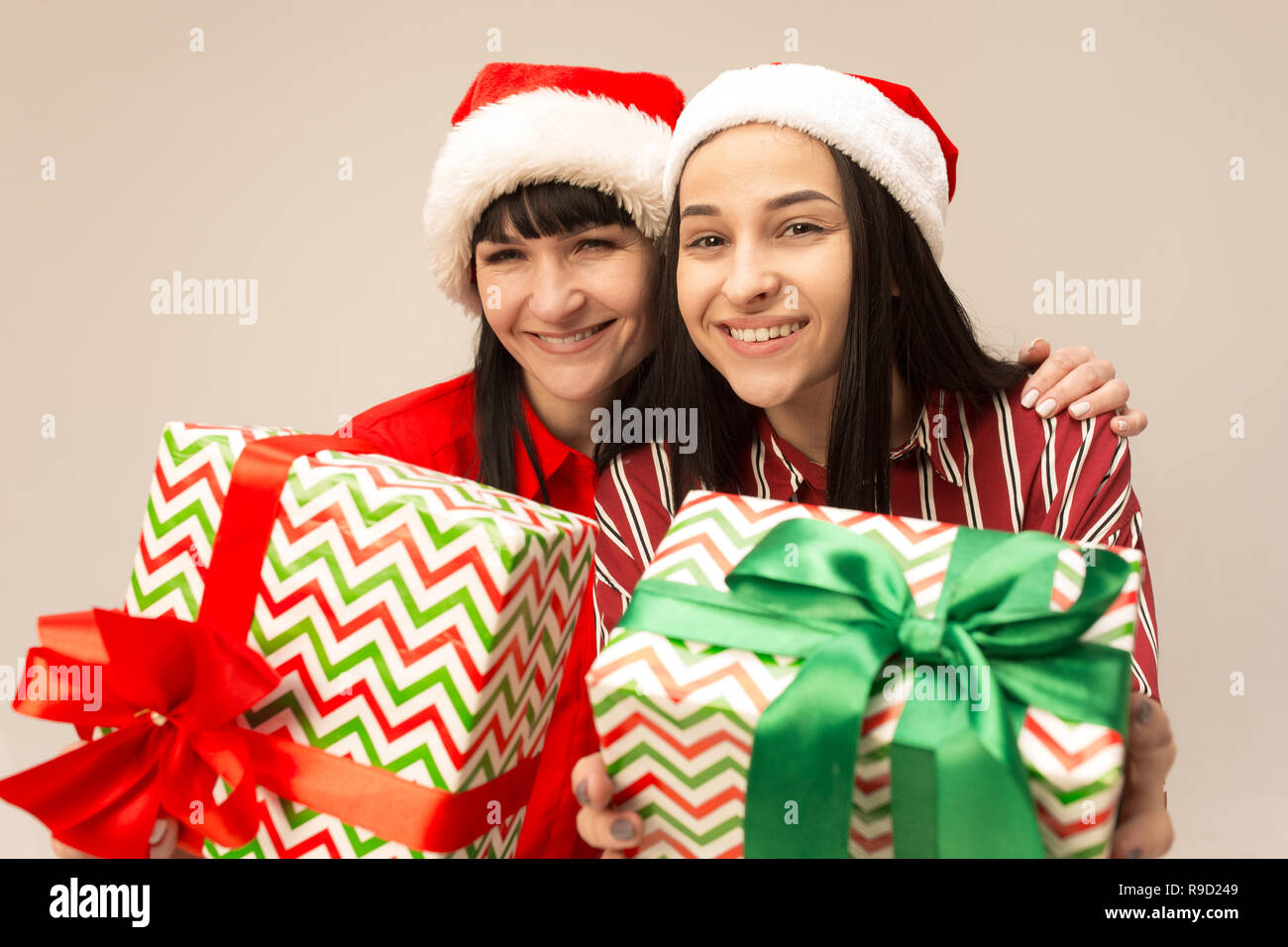 Happy family in Christmas sweater posing with gifts. Enjoying love hugs, holidays people. Mom and doughter on a gray background in the studio Stock Photo