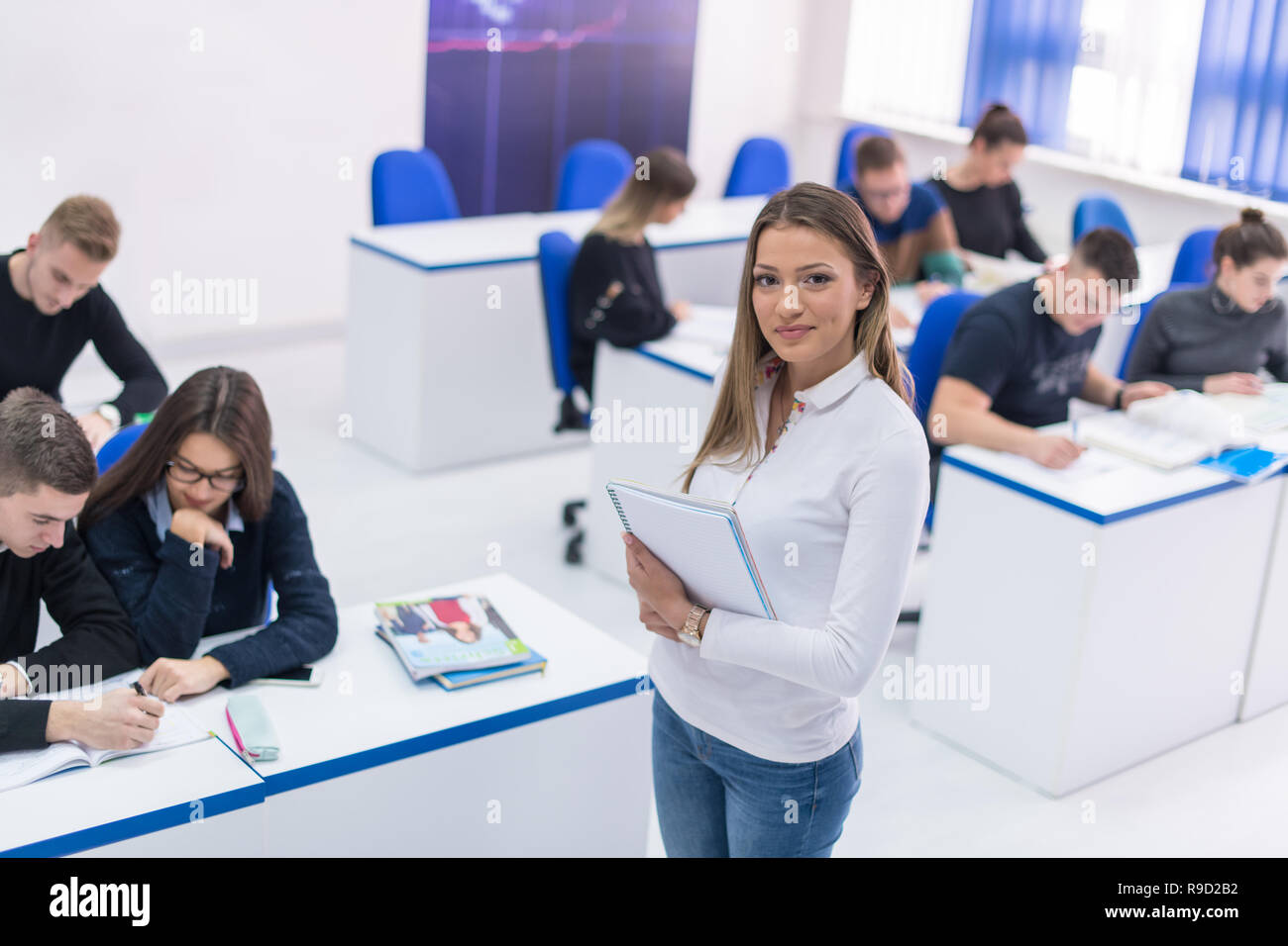young beautiful female student with others writing notes in the classroom Stock Photo