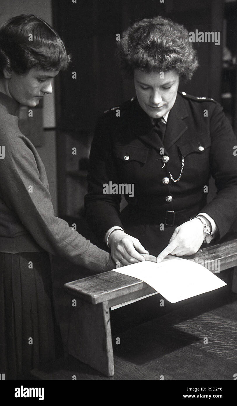 1950s, historical, a uniformed female police constable finger printing a young lady, England, UK. Fingerprint identification is an important criminal investigation tool due the fact that fingerprints are unique to an individual and do not change over time. Even identical twins have different fingerprints. Stock Photo