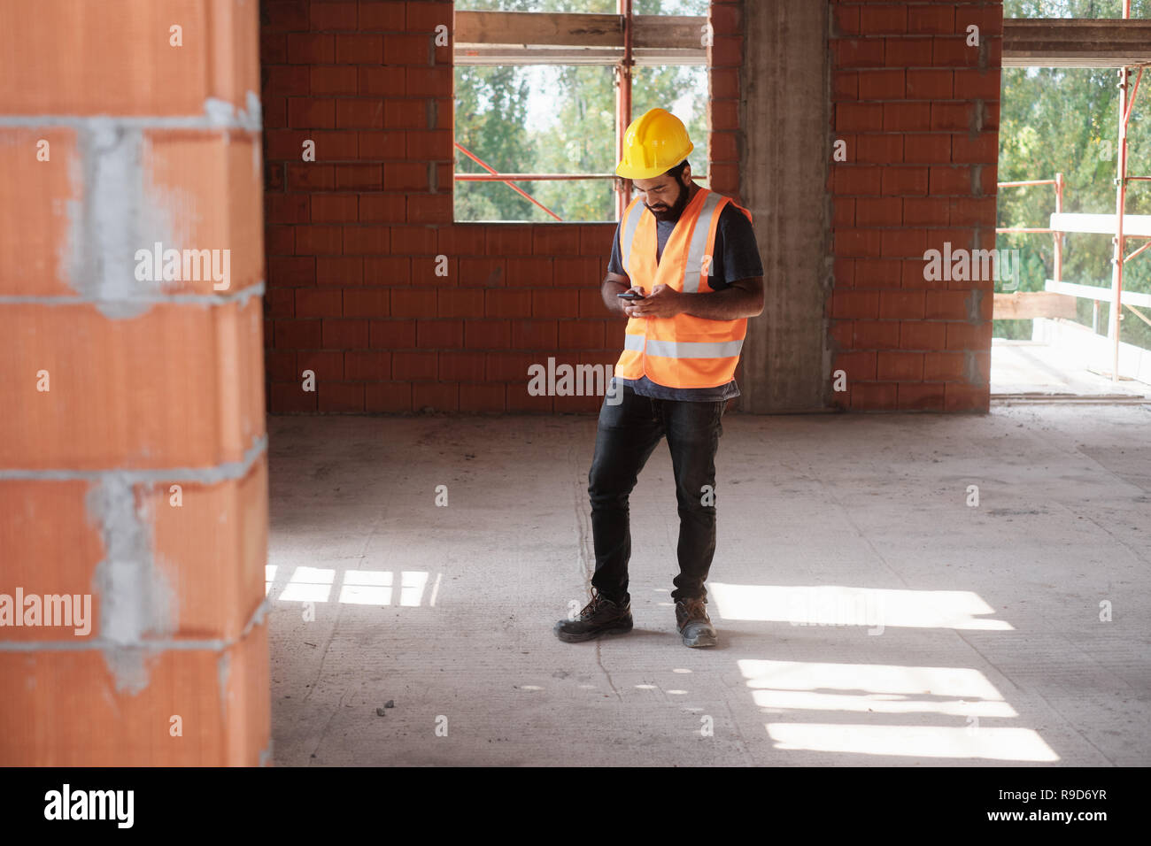 Man Working In Construction Site Smiling And Using Smartphone Stock Photo