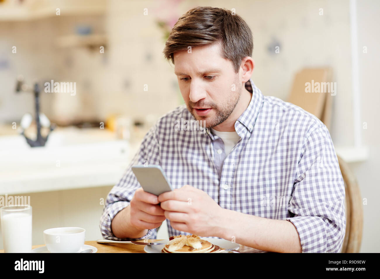 Concentrated man using smartphone at breakfast Stock Photo