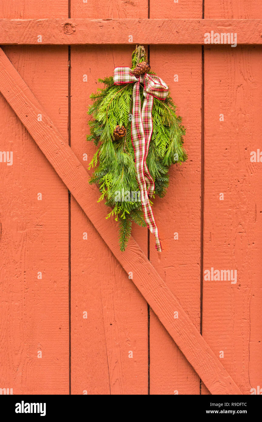 Traditional natural evergreen Christmas swag with plaid ribbon hung on painted orange wood fence. Stock Photo
