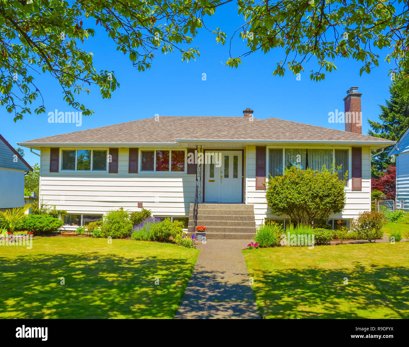 Average family house with green lawn and trees in front on blue sky