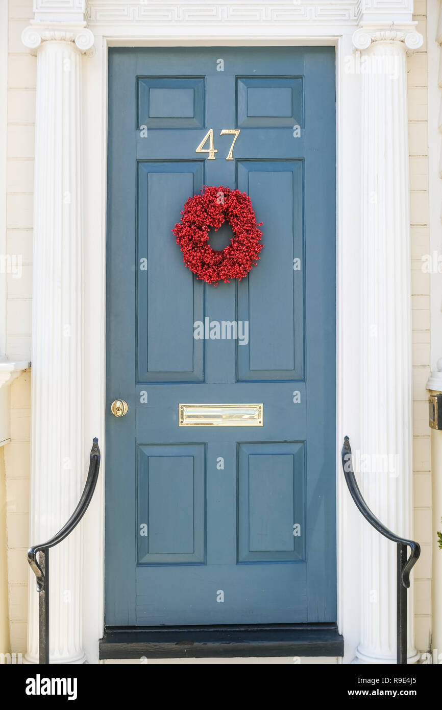 An understated traditional red popcorn berry Christmas wreath decorates the wooden door on a historic home for the holidays on Tradd Street in Charleston, South Carolina. Stock Photo